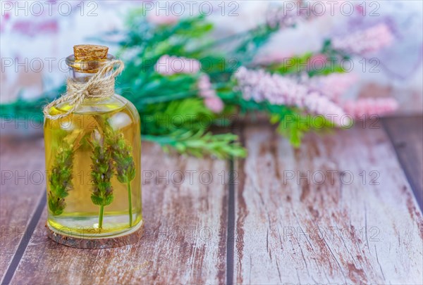 Glass bottle with lavender oil with lavender branches inside on a wooden table