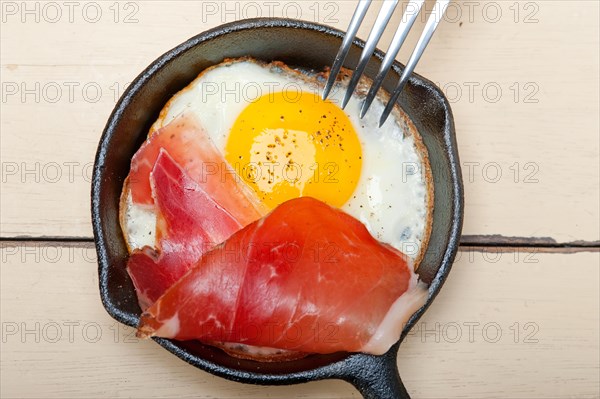 Fried egg sunny side up with Italian tyrolean speck smoked ham on a skillet