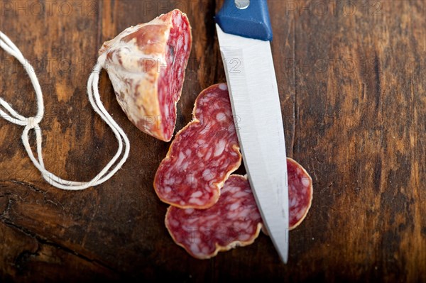 Slicing italian salame pressato pressed over old wood table