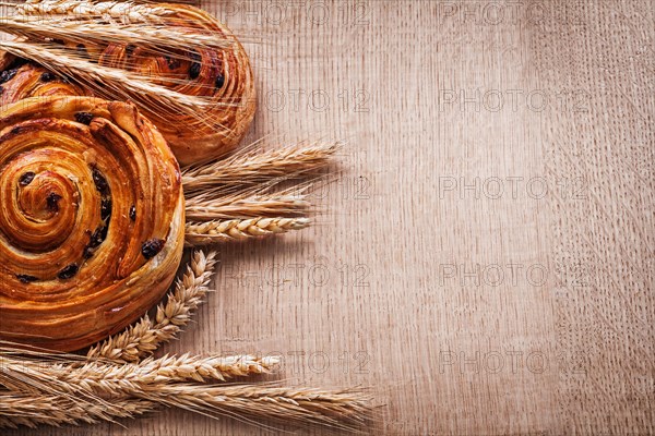 Bunches of golden wheat ears buns with sultanas on oak board Food and drink concept