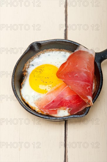 Fried egg sunny side up with Italian tyrolean speck smoked ham on a skillet