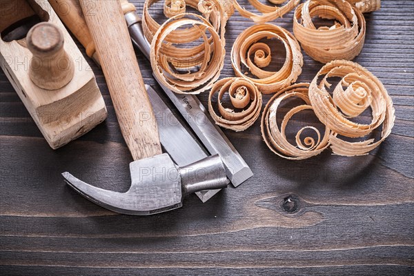 Close up picture of planer claw hammer metal chisel and wooden curled shavings on vintage wooden board building concept