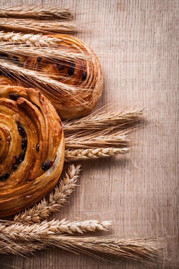 Bunches of golden wheat ears pastries with sultanas on oak board Food and drink concept