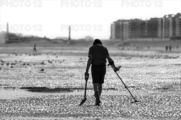 Man with metal detector beachcombing on sandy beach along the North Sea coast on an early morning in summer during the holiday season