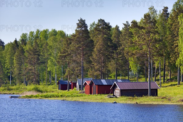 Red wooden boathouses along lake Siljan in summer