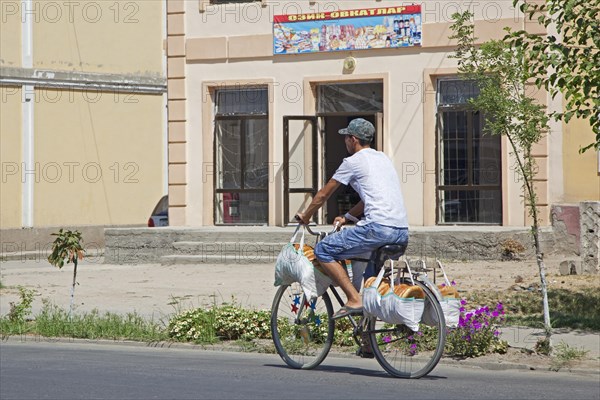 Uzbek man riding bicycle delivers traditional tandoor bread from bakery to houses in small town near Samarkand