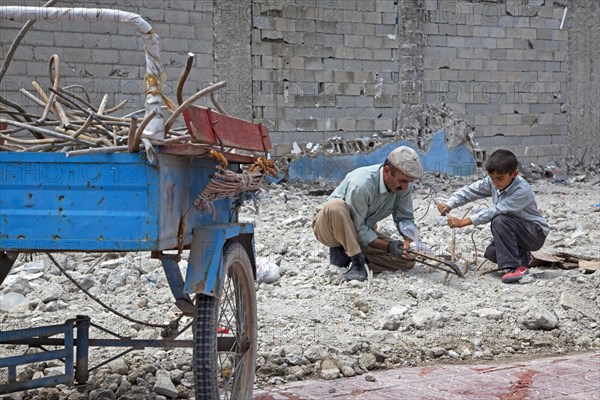 Son helping father recuperating iron with metal saw from debris of collapsed building after earthquake in Van