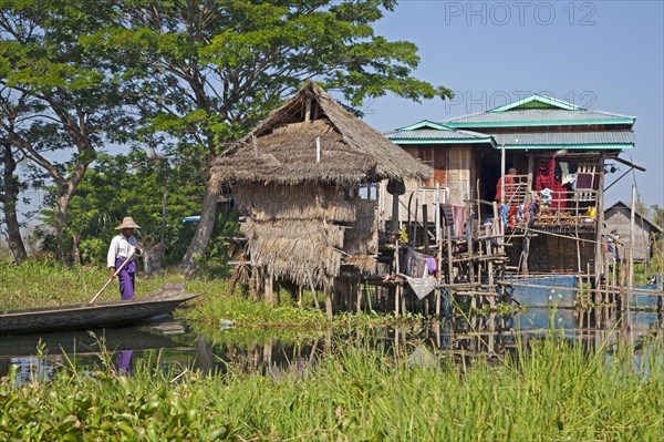 Intha man in proa at lakeside village with traditional bamboo houses on stilts in Inle Lake