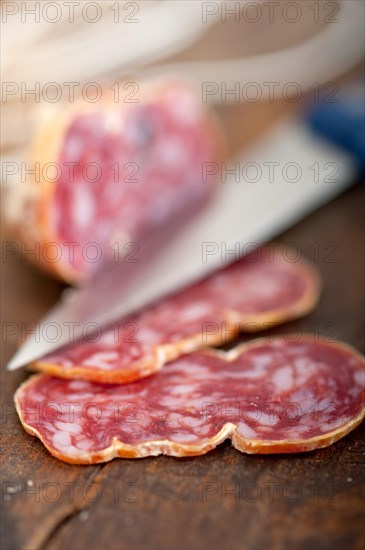 Slicing italian salame pressato pressed over old wood table