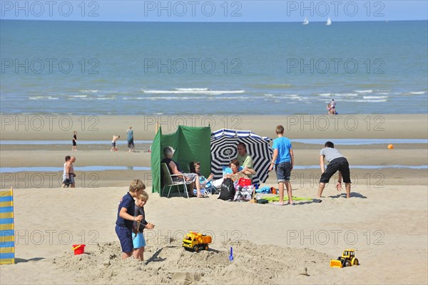 Sunbathers in summer sunbathing behind parasol and windbreak on beach along the North Sea coast at Koksijde