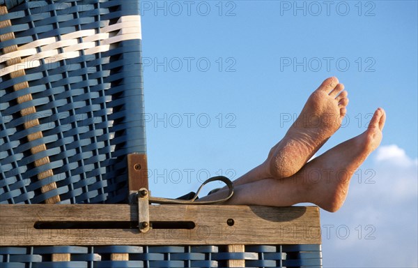 Bare feet sticking out from roofed wicker beach chair along the North Sea coast on the island Sylt