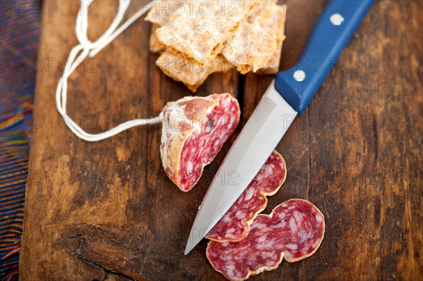 Slicing italian salame pressato pressed over old wood table