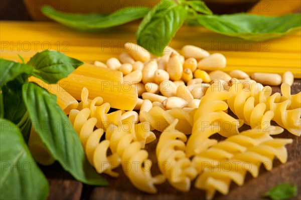 Italian basil pesto ingredients and raw pasta over old wood macro