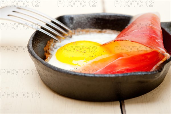 Fried egg sunny side up with Italian tyrolean speck smoked ham on a skillet