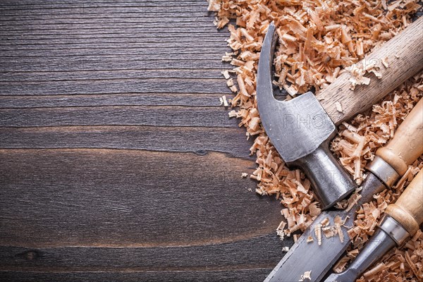 Horizontal view of claw hammer and metal flat chisel in wood shavings on vintage wooden panel Construction concept