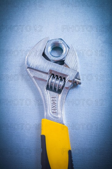 Adjustable spanner and stainless steel screw nut on a metallic background Design concept