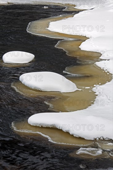 Brown slush ice along riverbank covered in snow in winter