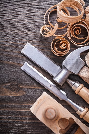 Planner claw hammer flat chisel and wooden curled shavings on vintage wooden board Building concept