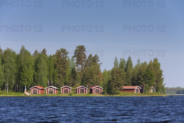 Red wooden boathouses along lake Siljan in summer