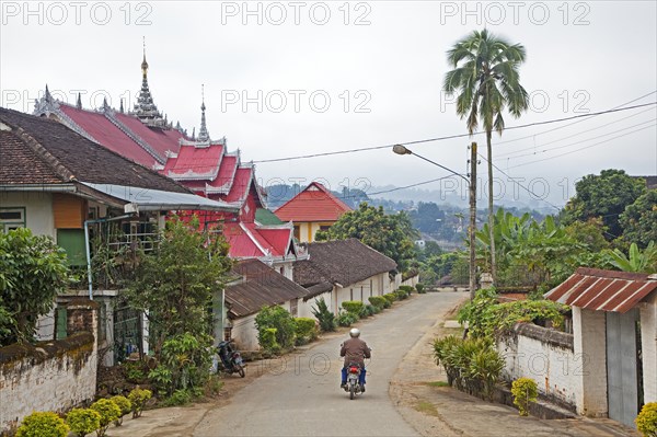 Motorcyclist riding past Buddhist temple in the town Keng Tung