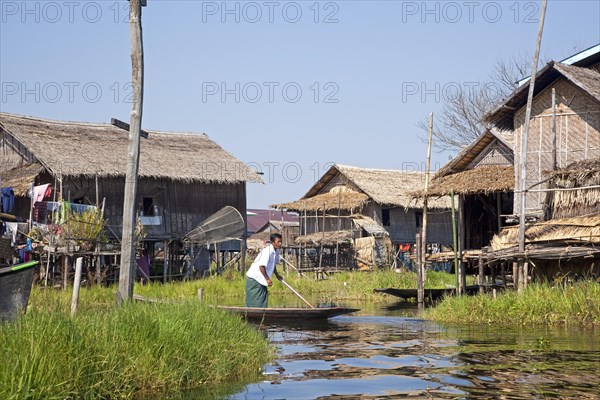 Intha man in proa at lakeside village with traditional bamboo houses on stilts in Inle Lake