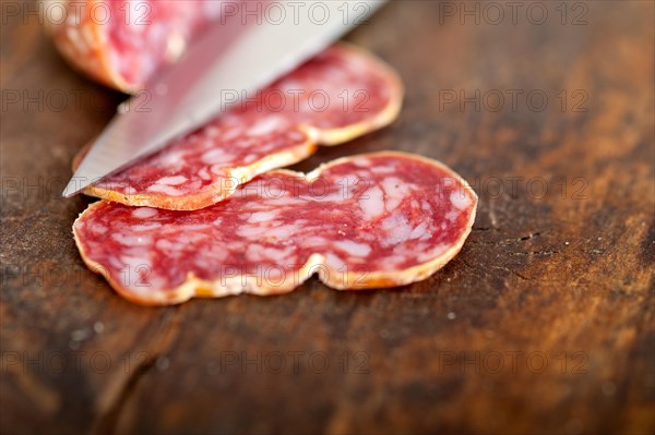 Slicing italian salame pressato pressed over old wood table