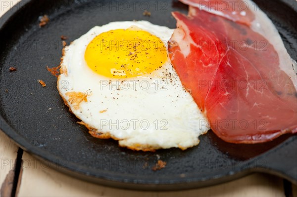 Fried egg sunny side up with Italian tyrolean speck smoked ham on a skillet