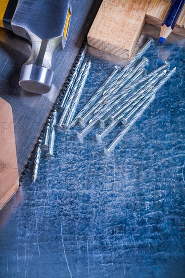 Construction nails claw hammer wooden bricks hand saw pencil on scratched metallic background maintenance concept