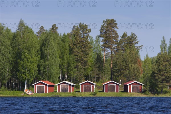 Red wooden boathouses along lake Siljan in summer