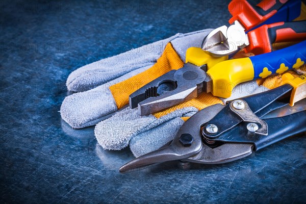 Safety gloves with pliers pliers and tin snips on scratched vintage metallic background construction concept