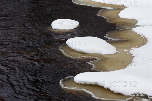 Brown slush ice along riverbank covered in snow in winter