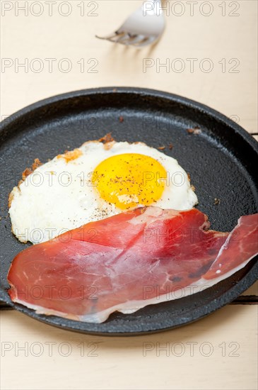 Fried egg sunny side up with Italian tyrolean speck smoked ham on a skillet