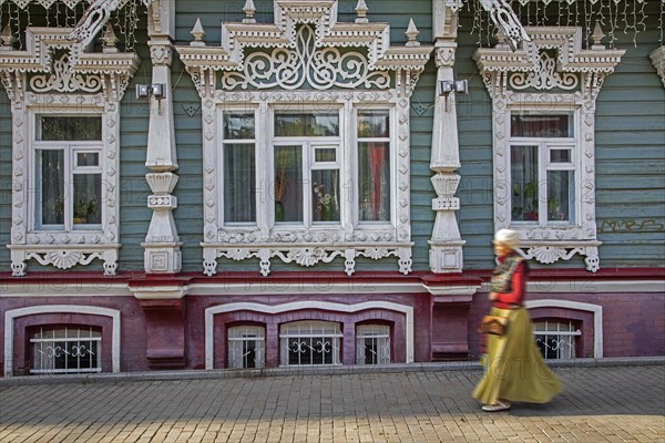 Russian woman walking in front of traditional ornate wooden house in the city Perm