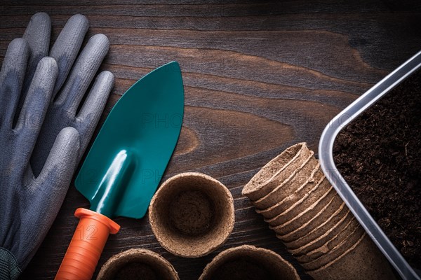 Hand shovel protection rubber gloves gardening tray with soil and peat pots on vintage wooden background agriculture concept