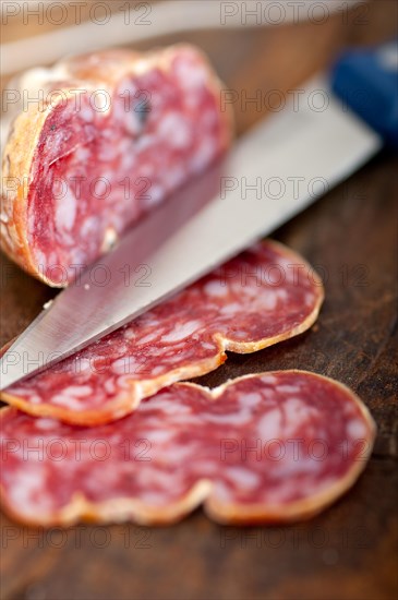 Slicing italian salame pressato pressed over old wood table