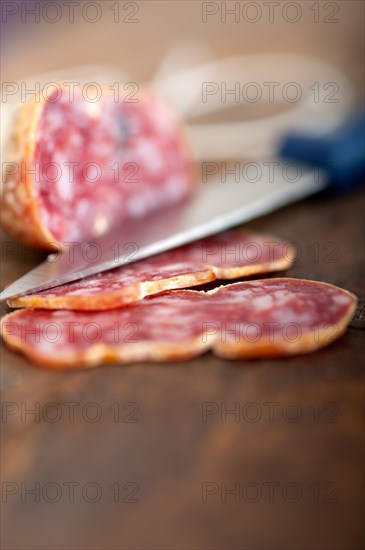 Slicing italian salame pressato pressed over old wood table