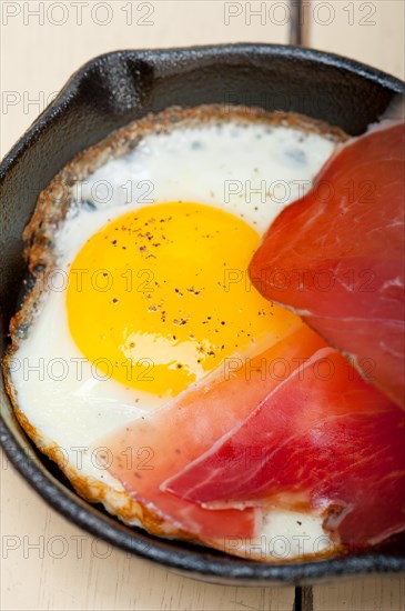 Fried egg sunny side up with Italian tyrolean speck smoked ham on a skillet