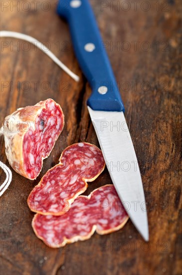 Slicing italian salame pressato pressed over old wood table