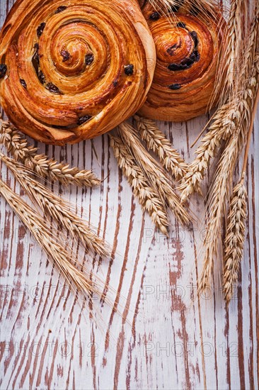 Freshly baked sultana rolls Wheat ears on a vintage wooden board Food and drink concept