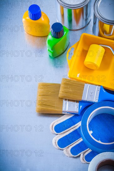 Household tapes safety gloves paint brushes roller tray cans and bottles on metallic background construction concept