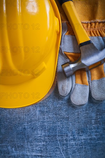 Protective gloves yellow building helmet and metal claw hammer on scratched metallic background maintenance concept