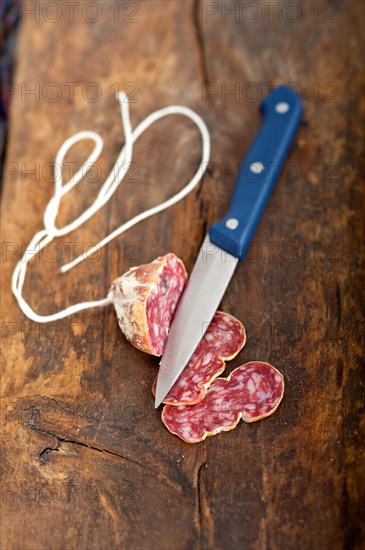 Slicing italian salame pressato pressed over old wood table