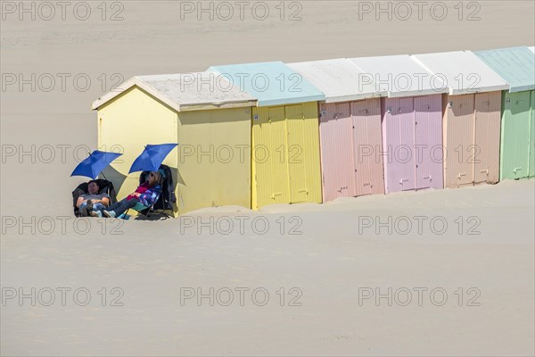 Two day trippers falling asleep under sunshades next to pastel coloured beach cabins at Berck