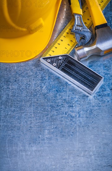 Hard hat claw hammer square ruler and adjustable spanner on scratched metallic background construction concept