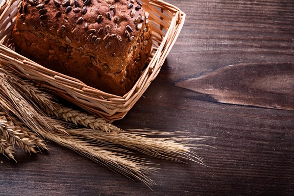 Crusty bread with seeds in wicker basket Wheat ears on vintage pine wooden board Food and drink concept