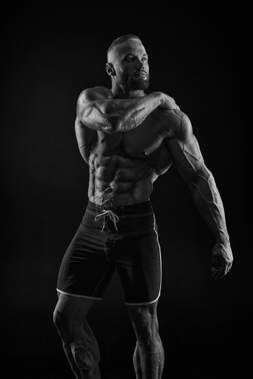 Silhouette of a strong bodybuilder. Confident young fitness athlete with a powerful body and perfect abs. Black and white photography. Dramatic light. Mixed media