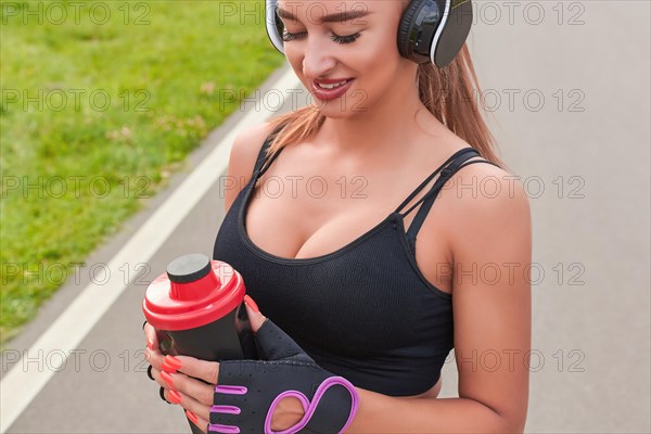 Girl posing with a sports nutrition shaker in the park. The concept of a healthy lifestyle. Sports Equipment. Fitness style advertisement. Mixed media