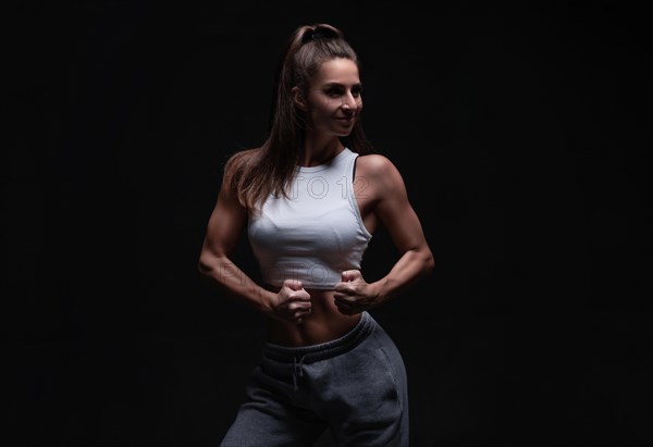 Athletic fitness woman posing in the studio on a dark background. Photo of an attractive woman in fashionable sportswear. Sports and healthy lifestyle. Mixed media