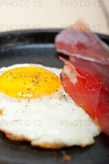 Fried egg sunny side up with Italian tyrolean speck smoked ham on a skillet