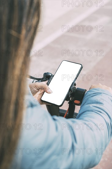 Top rear view of middle-aged latina woman in her 40s 50s with long hair and blue jacket riding electric scooter using smart phone